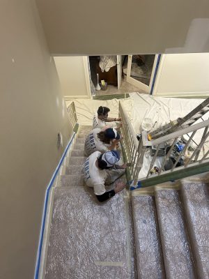 Three painters from Pearl Painters in Portland sit on plastic-covered stairs with painting supplies and tape, pausing during work.