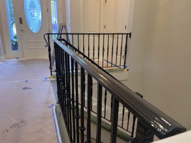 Painter finished black stair railing in a home entryway; floors and stairs are covered for protection by Pearl Painters, Portland.