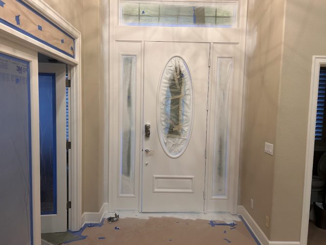 A painter from Pearl Painters in Portland is painting a front door and sidelights white, with plastic and tape covering glass.