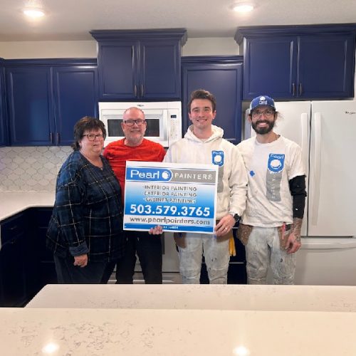 Four people in a kitchen with blue cabinets; two painters hold a Pearl Painters sign. Portland painting company.