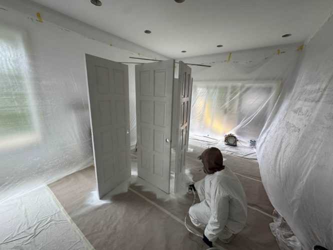 A painter from Pearl Painters in Portland expertly spray paints doors white in a plastic-covered room.