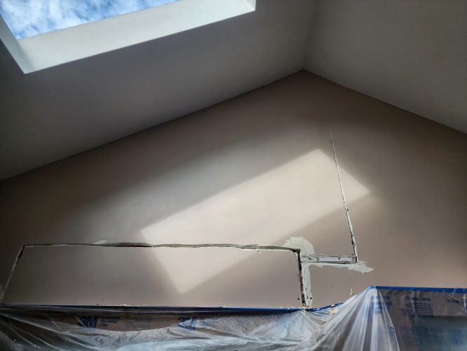 A Portland room prepped for painting by Pearl Painters: vaulted ceiling, skylight, plastic covers, patched wall hole.
