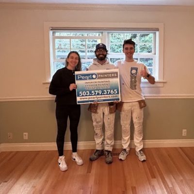 Three people in a newly painted room, two in painter uniforms, hold a Pearl Painters painting company sign. Likely Portland.