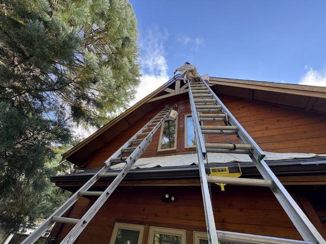 A Pearl Painters painter on a ladder painting wood house eaves.