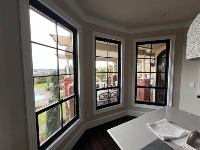 A room with three large windows overlooks a patio, pool, and landscaped area in West Linn