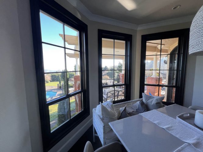 Interior view featuring three large black-framed windows that overlook a patio and pool. A table with a white runner and cushioned seating is visible