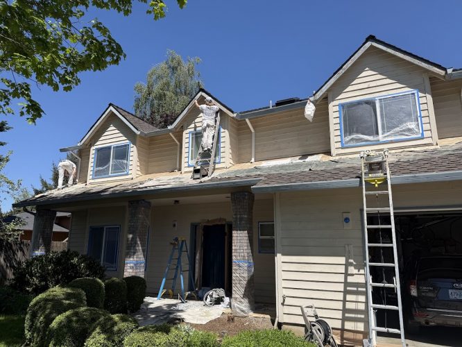 Painters from Pearl Painters paint a beige two-story house exterior in Portland using ladders and scaffolding on a sunny day.