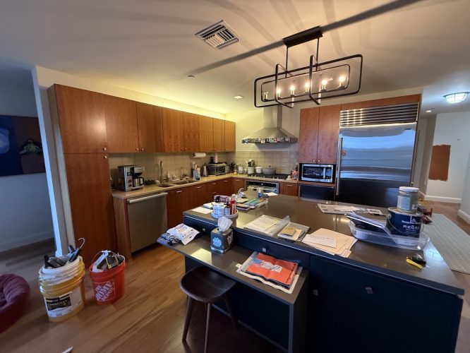 A painter's tools are scattered in a modern Portland kitchen with wood cabinets, stainless appliances, and an island with stools.