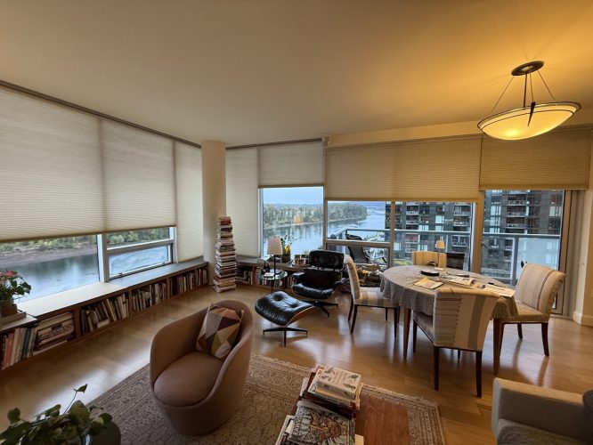 Modern Portland apartment living room with large windows, bookcases, armchairs, dining table, and city-water view; painter’s work by Pearl Painters.