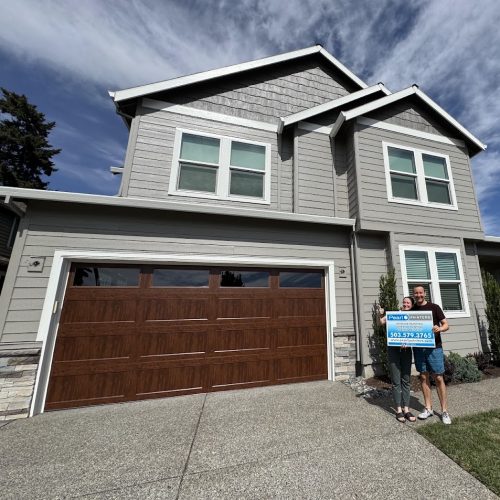 A man and woman hold a Pearl Painters sign in front of a gray two-story house.
