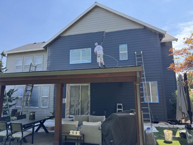 A Pearl Painters painter spray painting a dark blue house in Portland.