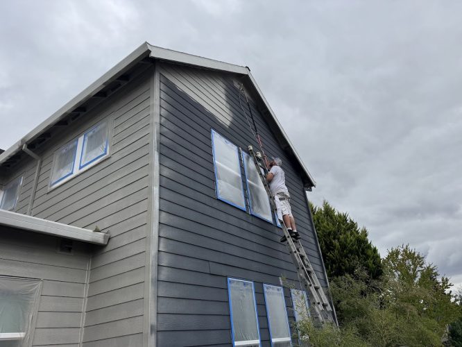 A Pearl Painters painter on a ladder painting a house gray in Portland.