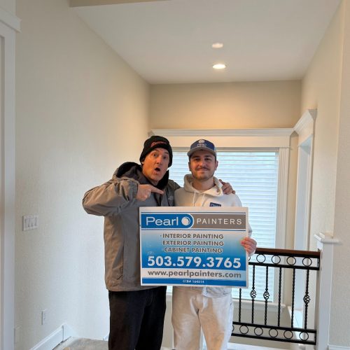 Two people indoors; one in work clothes holds a Pearl Painters painting services sign with contact info, likely in Portland.