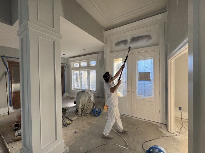 A painter in protective gear uses a spray gun to paint an interior wall; house under renovation, Portland, Pearl Painters.