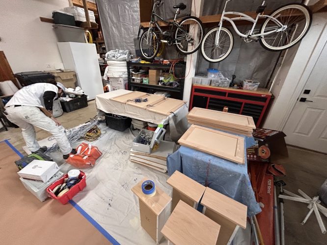 A painter sorts tools in a garage with cabinets, bikes, and painting materials. Pearl Painters, Portland.