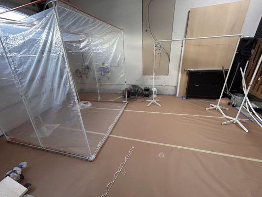 Plastic enclosure and frame in room with brown floor, tape lines; painter's tools nearby. Pearl Painters, Portland.