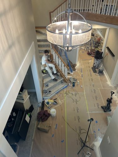 A painter for Pearl Painters sits on a staircase in Portland, with tools and protective paper on the floor below a large light.