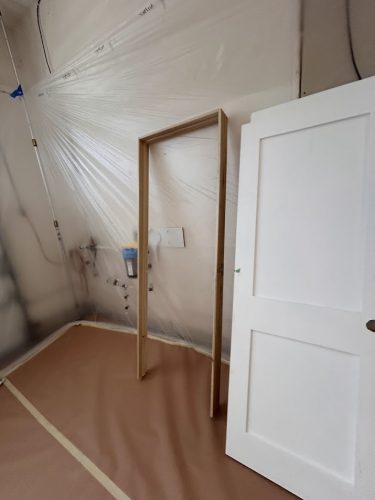 A white door and wooden frame lean on a plastic-covered wall in a room being painted by Pearl Painters in Portland.