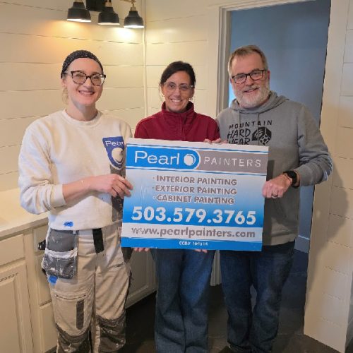 Three people in a kitchen hold a Pearl Painters sign for Portland painting services: interior, exterior, and cabinet.