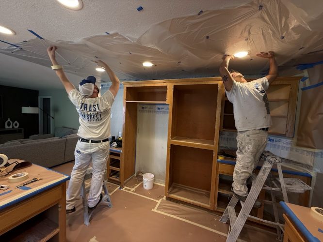 Two painters from Pearl Painters in Portland use ladders to cover a ceiling with plastic before painting.
