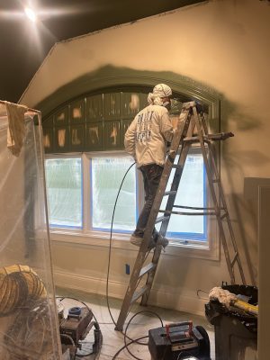 A Pearl Painters painter in Portland paints green around a masked arched window, with the room also masked for protection.