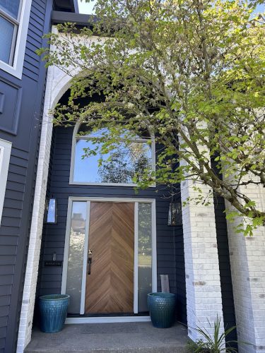 Trusley house entrance painted by Pearl Painters; chevron door, arched window, blue planters, tree visible. April 2026.