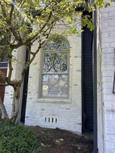 Large arched window in white brick Trusley house, greenery in front; painter from Pearl Painters, Portland, April 2026.