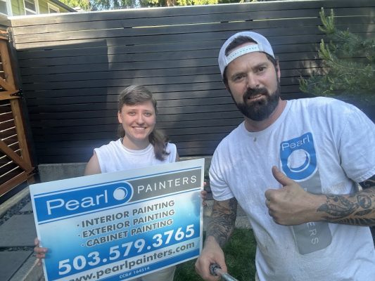 Two people outdoors in Portland holding a Pearl Painters painting sign; one gives a thumbs up.