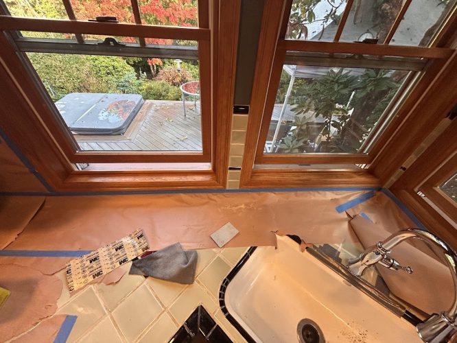 Kitchen sink and tiled counter masked with paper and tape for painting by Pearl Painters, under windows facing patio and garden.
