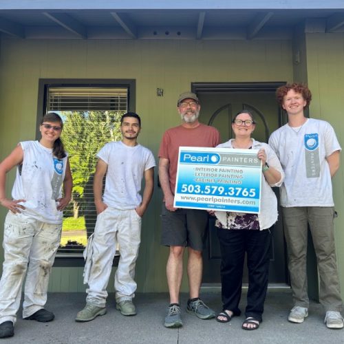 Five people stand in front of a painted house in Portland; two hold a Pearl Painters painting company sign. Four are dressed as painters, one is in casual clothes.