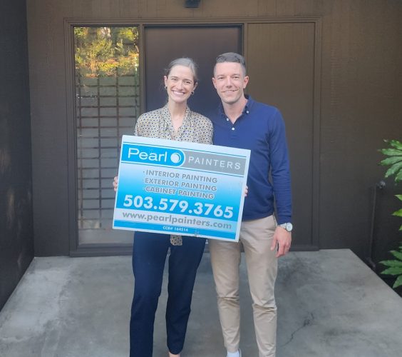 Two people outside a building in Portland hold a Pearl Painters sign advertising painting services with contact info.