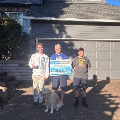 Three people and a golden retriever with a Pearl Painters sign stand outside a gray Portland house; painting contact info visible.