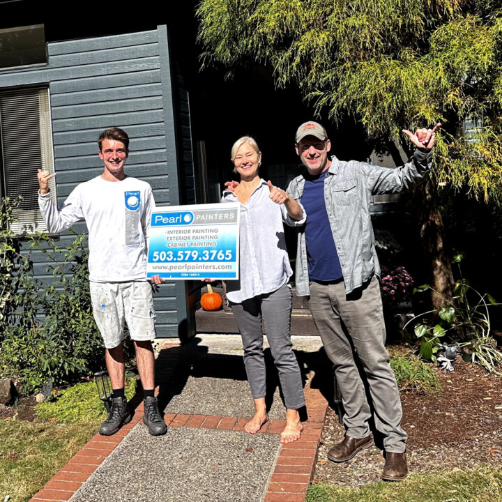 Three people hold a Pearl Painters sign for painting services outside a house, likely in Portland.