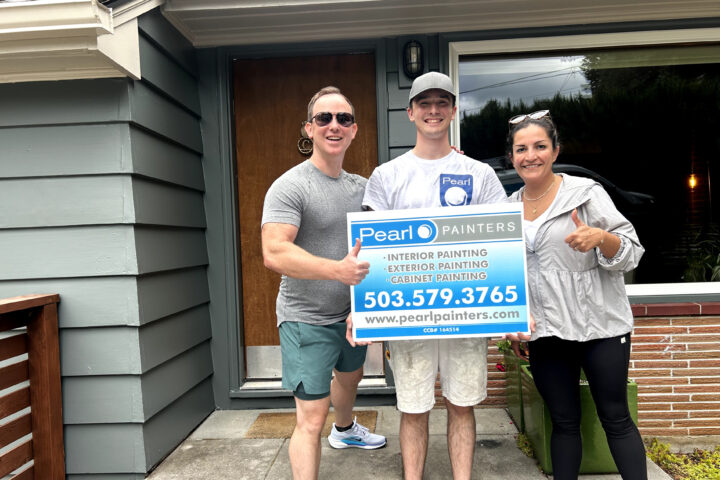 Three people outside a house in Portland hold a Pearl Painters sign showing painting services and contact info.
