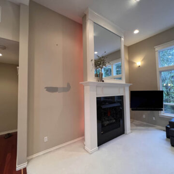 A living room with a white fireplace, hardwood floors, and large windows offering a view of trees outside underwent an interior painting project in Tigard that brightened the space.