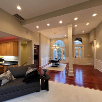 Spacious living room with red hardwood floors, beige walls, and arched doorways, featuring a kitchen area to the left and a seating area with a dark sofa.