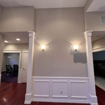 Interior painting project in Tigard that brightened the space, showing a wall with wainscoting and two wall-mounted lights, with doorways leading to adjacent rooms.