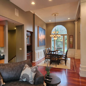 Elegant interior painting project in Tigard, featuring a living area with a couch and coffee table in the foreground, and a dining area with a table set against a backdrop of large windows and artwork on