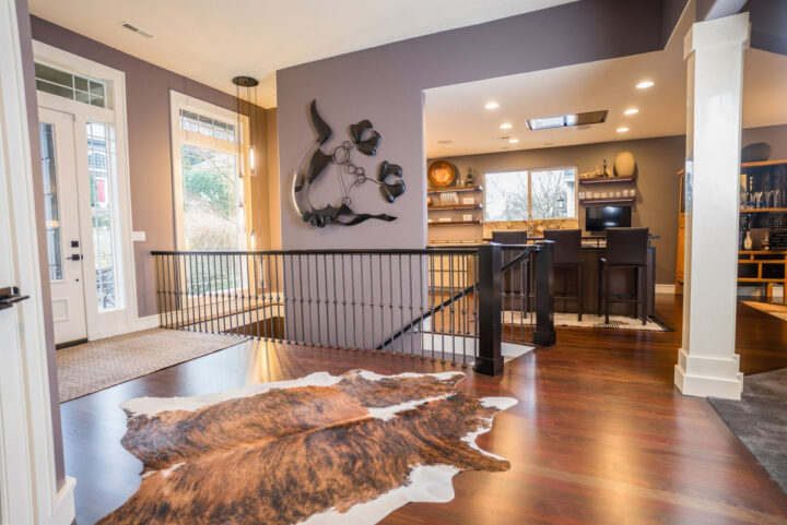 Modern home interior featuring an entryway with a cowhide rug, a metal railing, and a sculpture on the wall; kitchen visible in the background with new flooring installation.