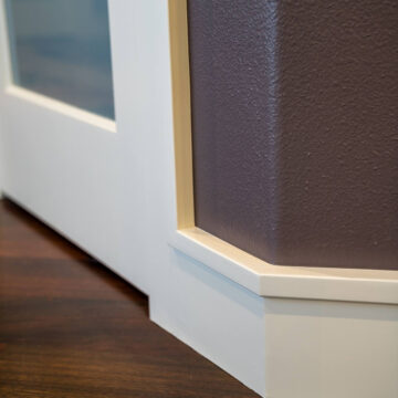 Close-up view of a white door frame against a dark brown wall, meeting a polished wooden floor.