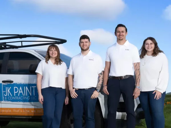 Four painters in white shirts and blue pants stand by a "JK Paint & Contracting LLC" vehicle outdoors in Portland.