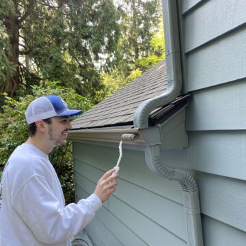 A man performing an exterior paint job on a house in Summer 2023.