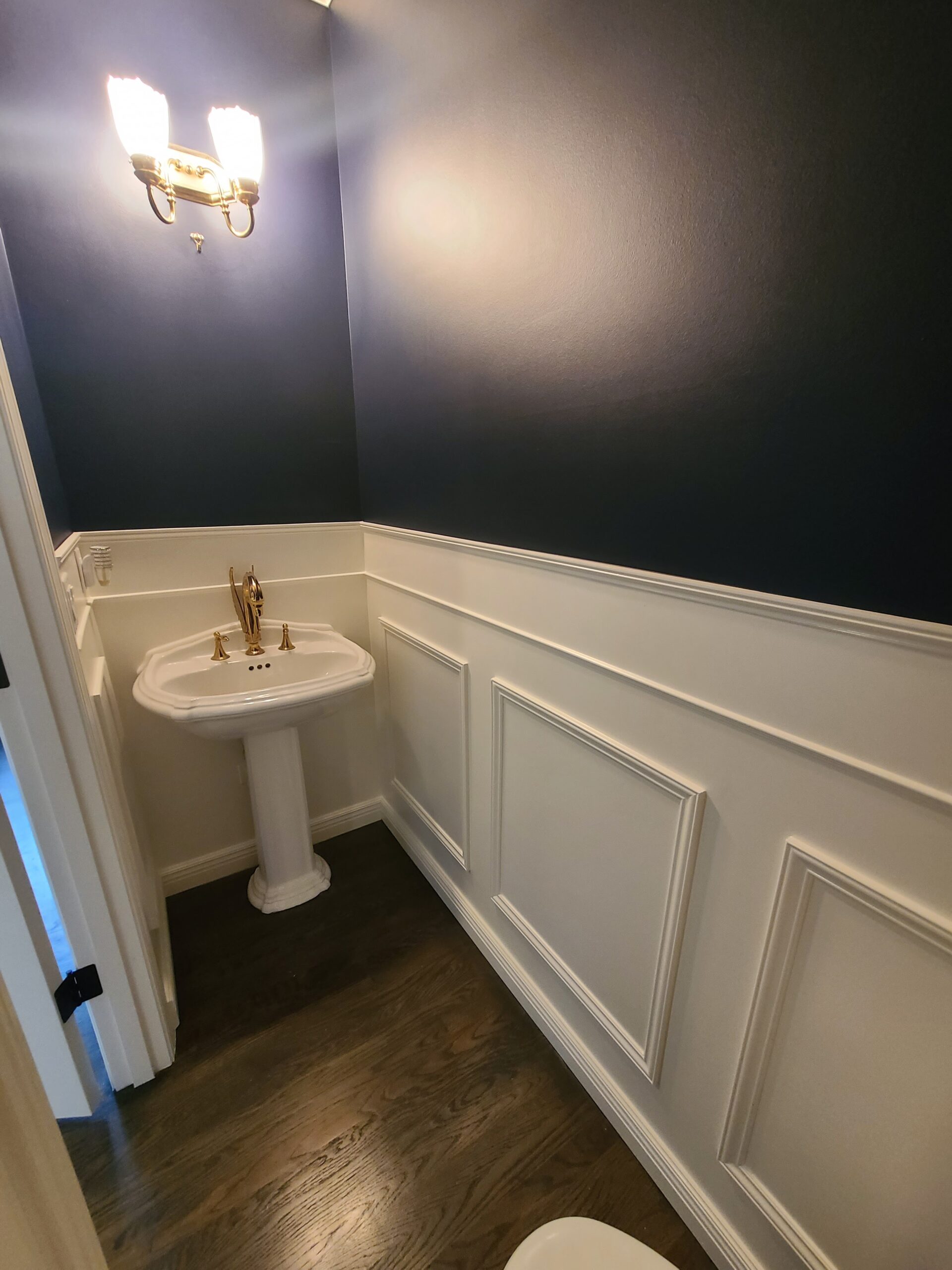 half bathroom freshly painted in dark blue with white wainscoting
