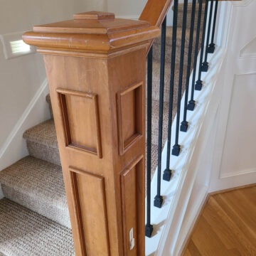 A wooden staircase with black metal railings, carpeted steps, and illuminated wall lights.