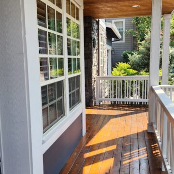 A wooden porch with a white railing and windows in the Whitford Neighborhood of Portland undergoes a fresh transformation.