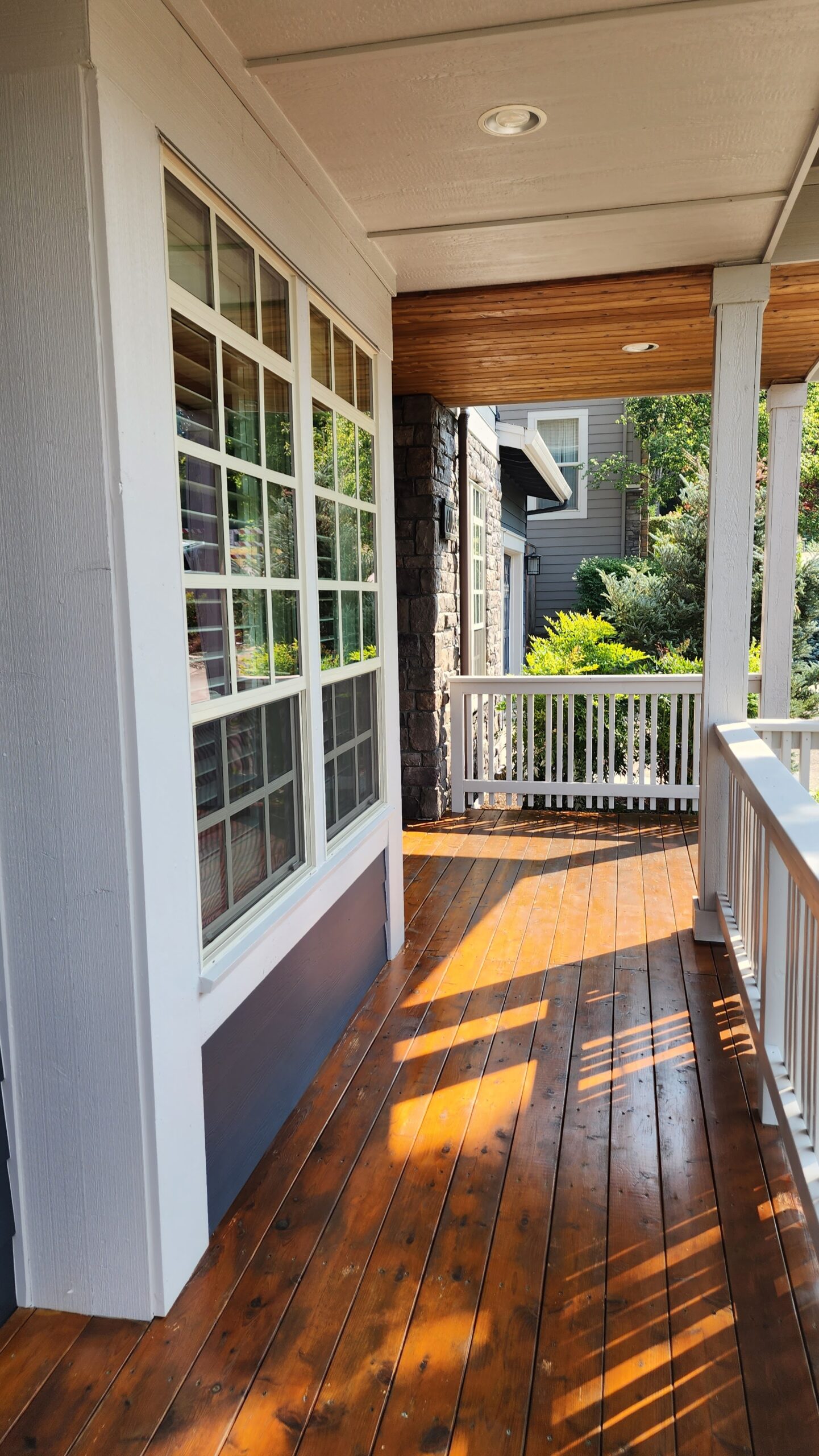 A wooden porch with a white railing and windows in the Whitford Neighborhood of Portland undergoes a fresh transformation.