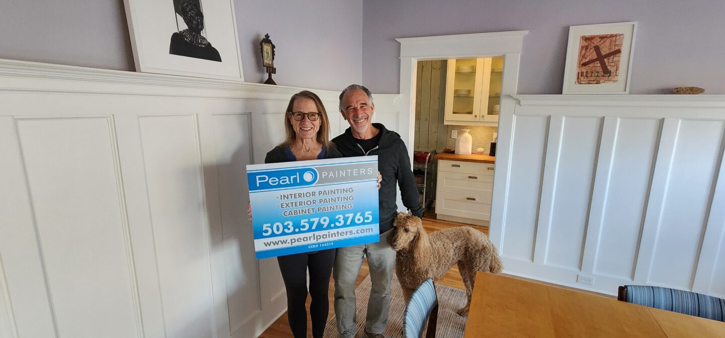 Two people standing in a living room with a Pearl Painters sign.