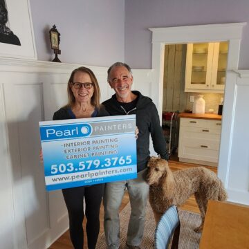 Two people standing in a living room with a Pearl Painters sign.