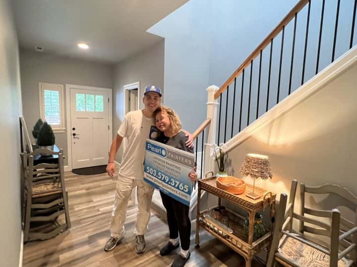 A couple in West Linn standing in front of a staircase holding a check for interior paint services for their home.