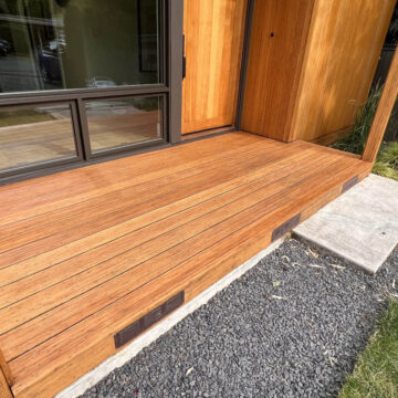 A newly built wooden deck with a sliding glass door, adjacent to a gravel walkway and grass lawn.